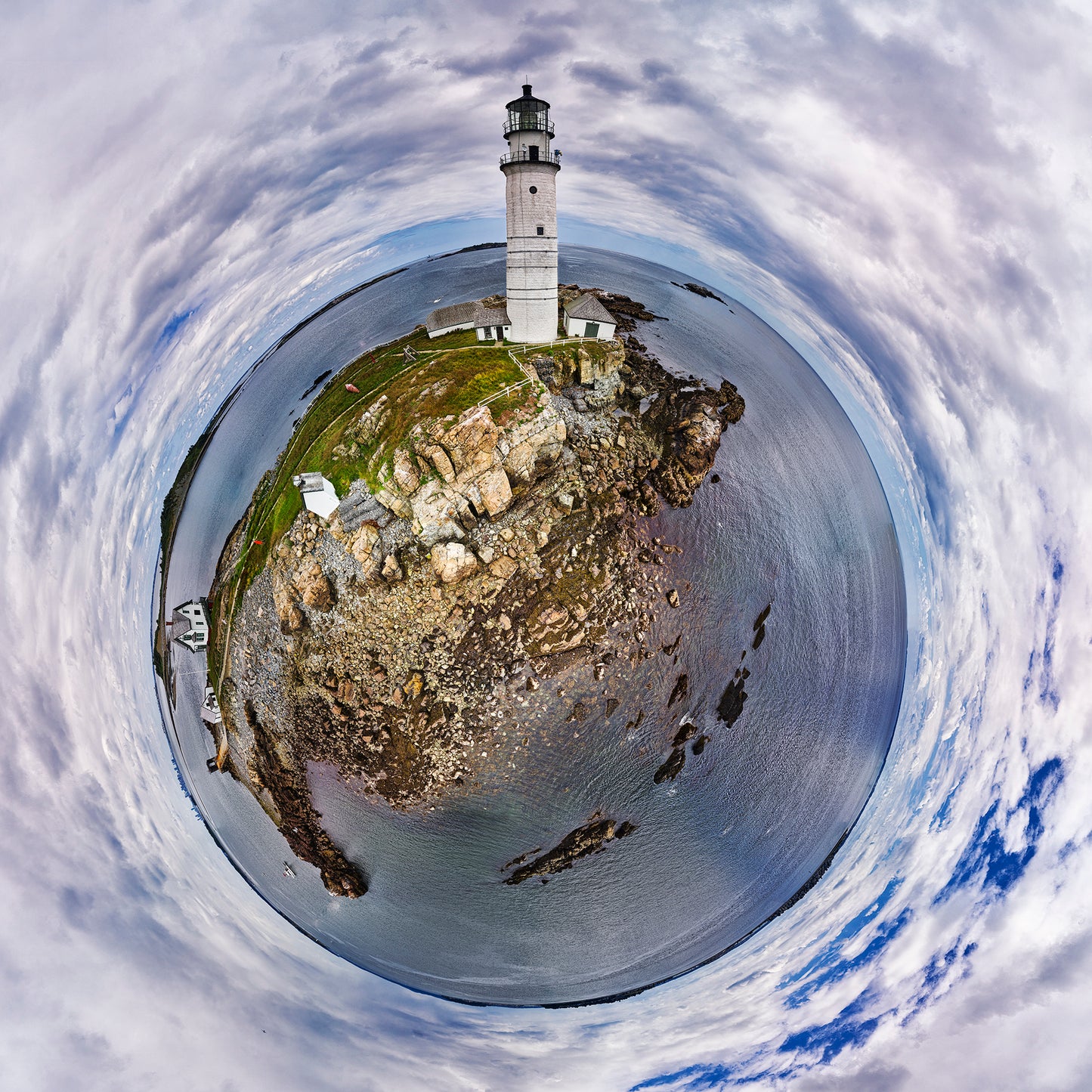 A 360-degree panoramic photograph of Boston Harbor Light, showing a circular view of the white lighthouse atop a rocky island with winding paths, small buildings, and a dramatic cloudy sky swirling overhead.