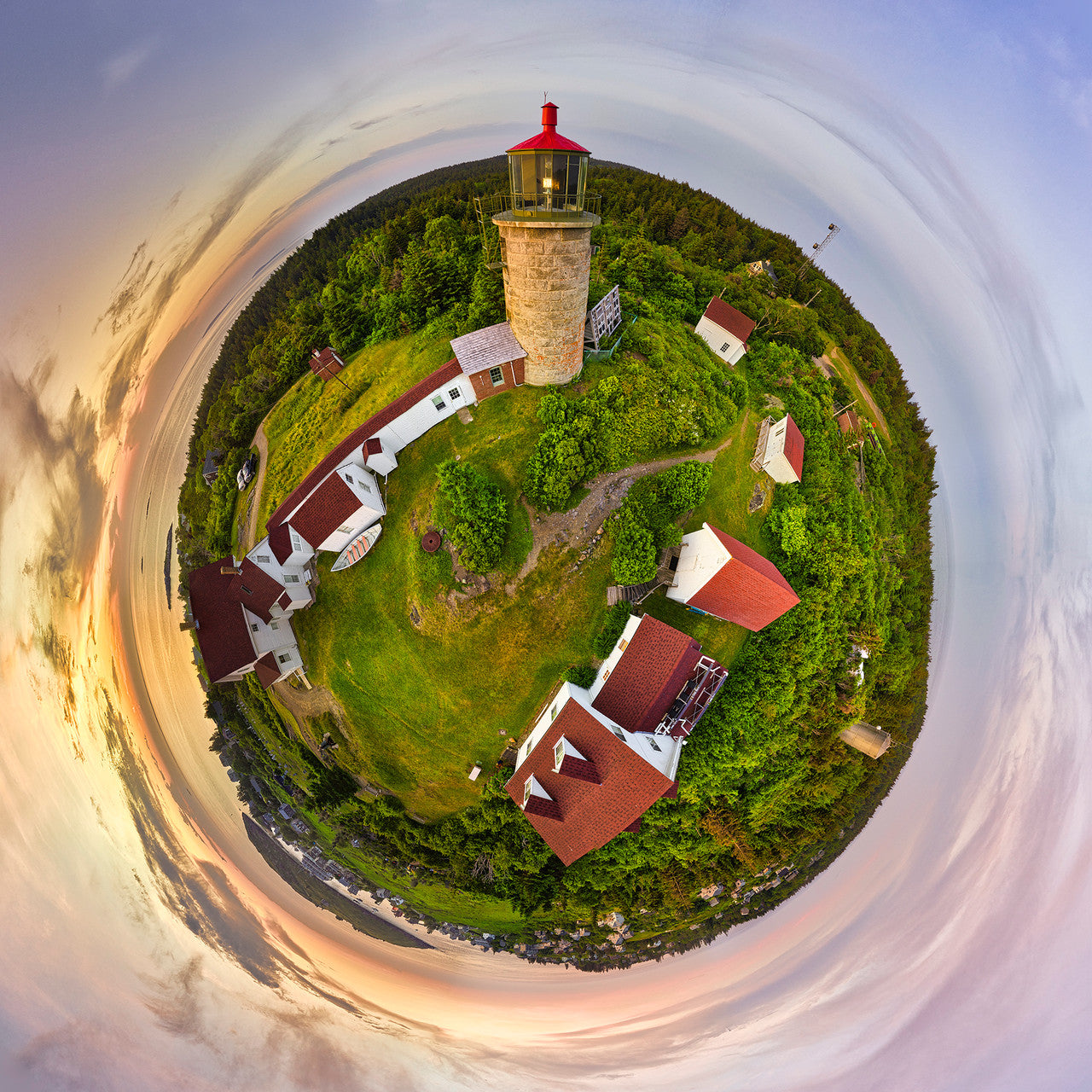 A 360-degree panoramic photograph of Monhegan Lighthouse at sunset, showing a circular view of the island with the lighthouse, surrounding buildings, lush greenery, and a golden sky.