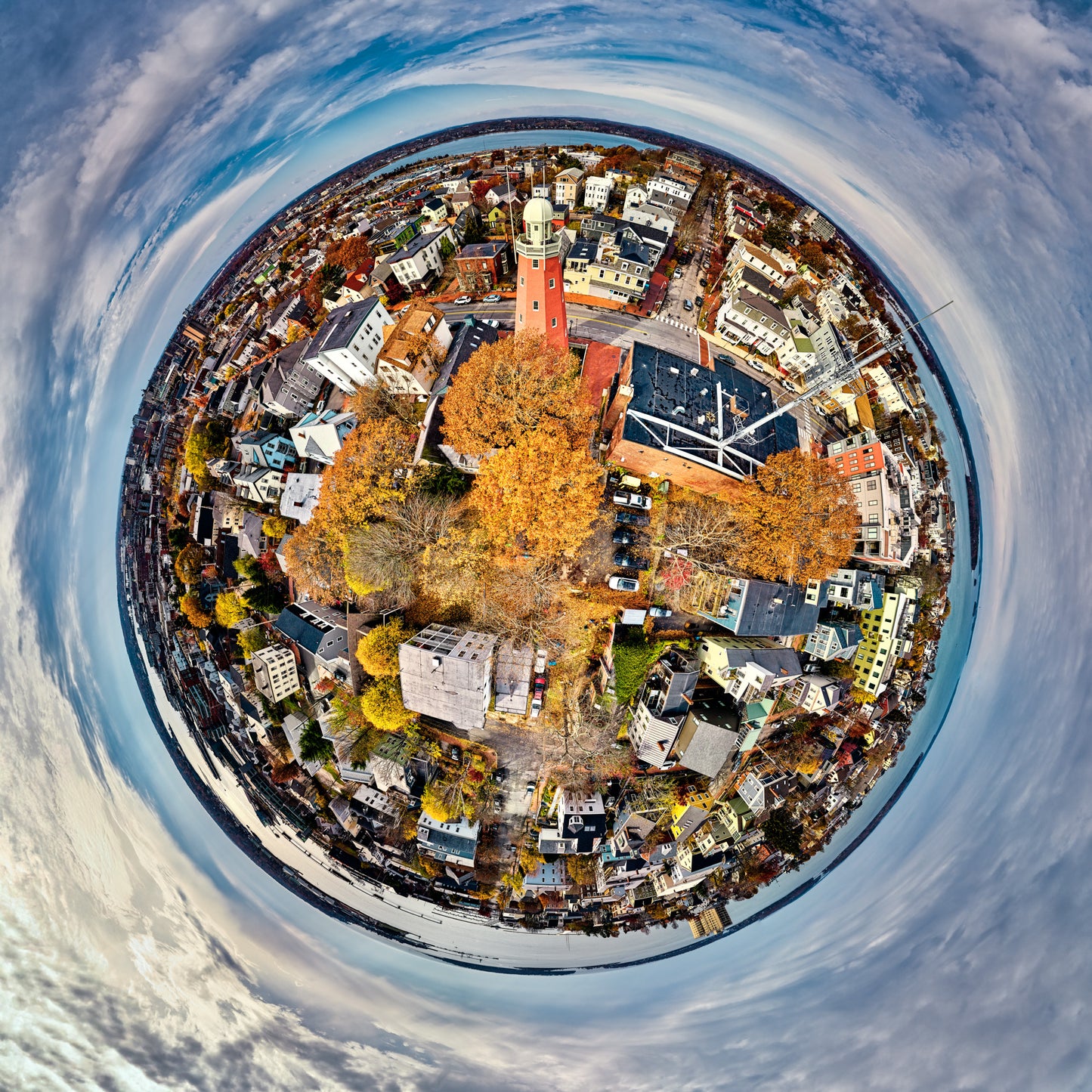 360-degree “tiny planet” image of Munjoy Hill in Portland, Maine, with the red Portland Observatory tower and autumn trees at the center, surrounded by houses, streets, harbor, and a circular blue-gray sky.