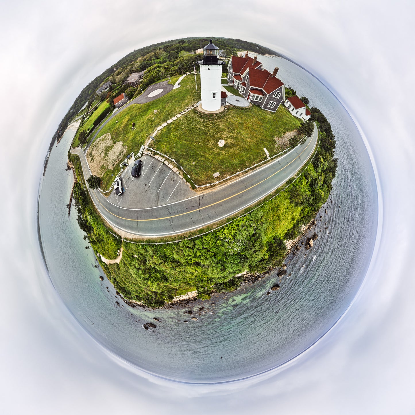 Alt text:
360-degree “tiny planet” image of Nobska Light, with the white lighthouse and red-roofed keeper’s house on a grassy hill, a curving coastal road, parking area, trees, and surrounding ocean wrapped into a small circular world under a soft gray sky.