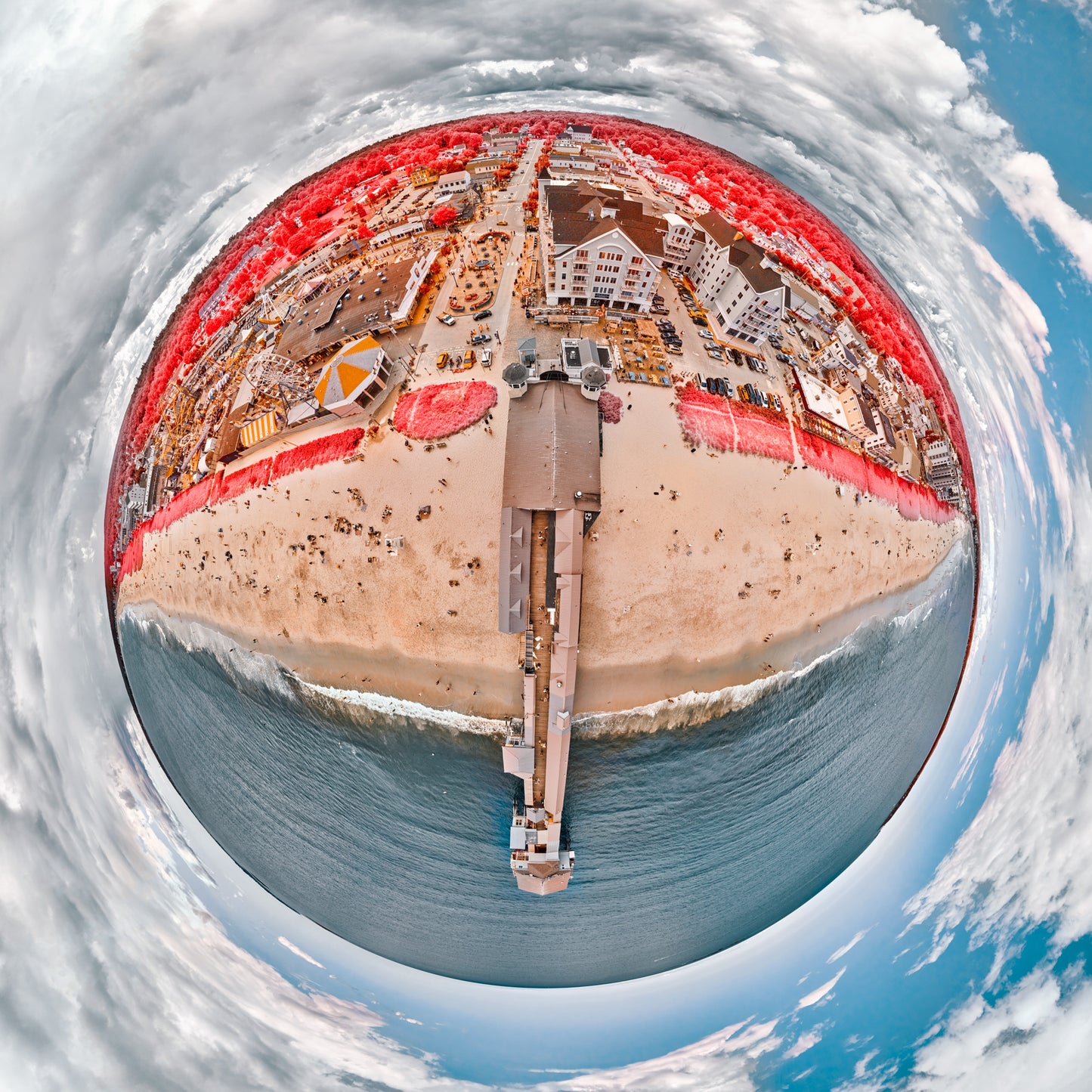 Spherical panoramic infrared photograph of Old Orchard Beach, featuring the iconic pier extending into turquoise waters, surrounded by crimson-colored vegetation and beachfront architecture under a dramatic sky.