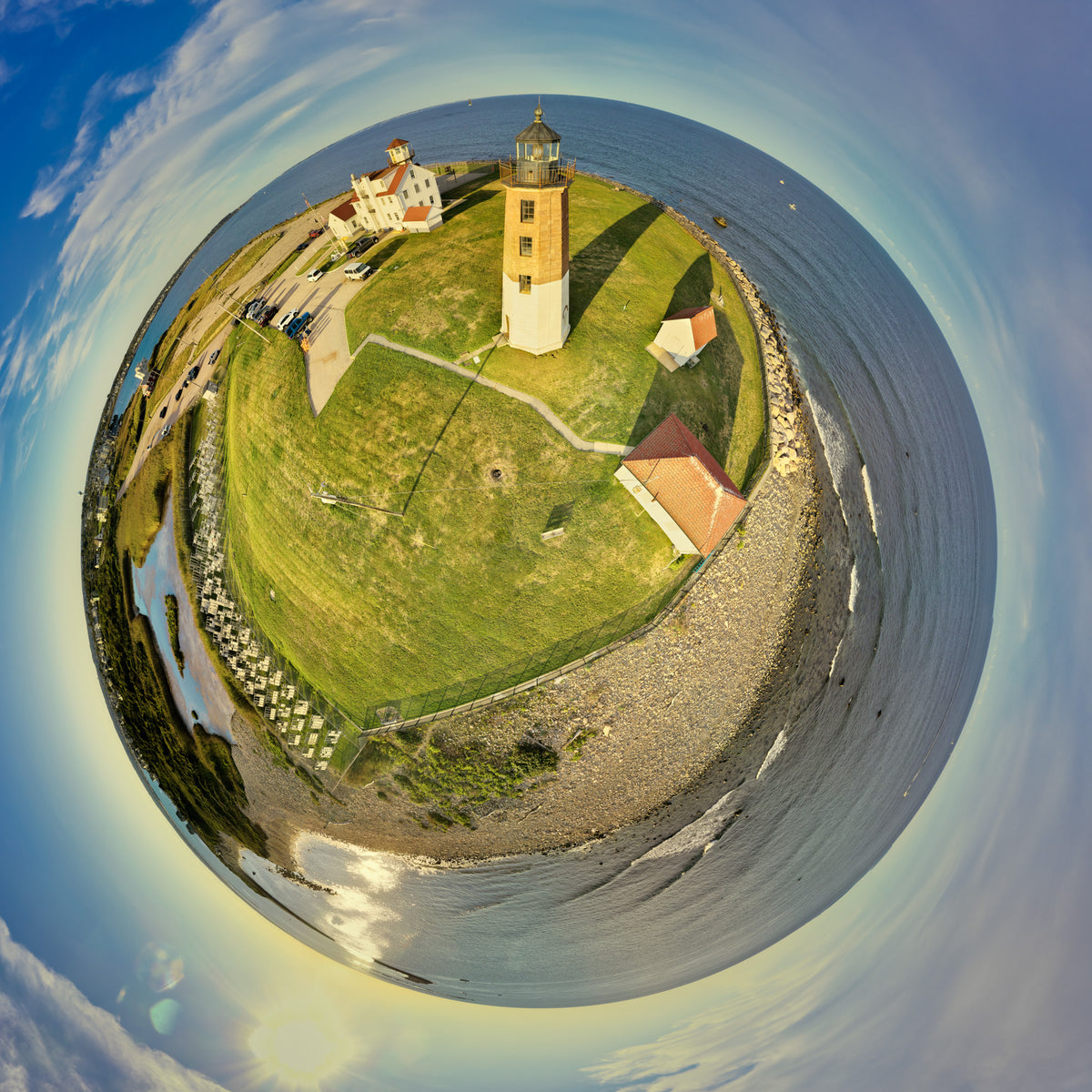 Aerial 360-degree Spherescape of Point Judith Light Station in Rhode Island, with the lighthouse and historic buildings curved into a tiny planet surrounded by blue Atlantic water beneath a sweeping sky and warm late-day sunlight.