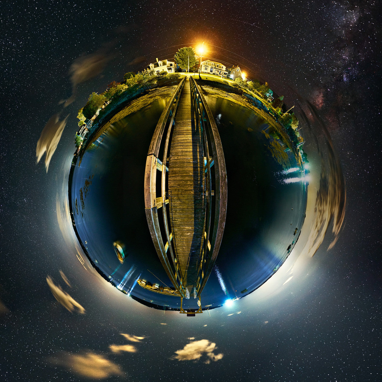 A 360-degree nighttime panoramic Spherescape showcasing Harpswell Town Wharf in Harpswell, Maine, with the galaxy's majesty unfolding above and the soft artificial lights of civilization below, captured in a palette of deep space blues, warm amber, and jet black.