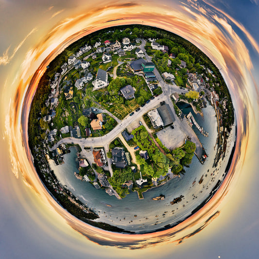 360-degree aerial panoramic photograph of Stonington, Maine, capturing the coastal town's essence with houses and roads encircling the harbor, against a dramatic backdrop of the sunset sky, in a spherical perspective.