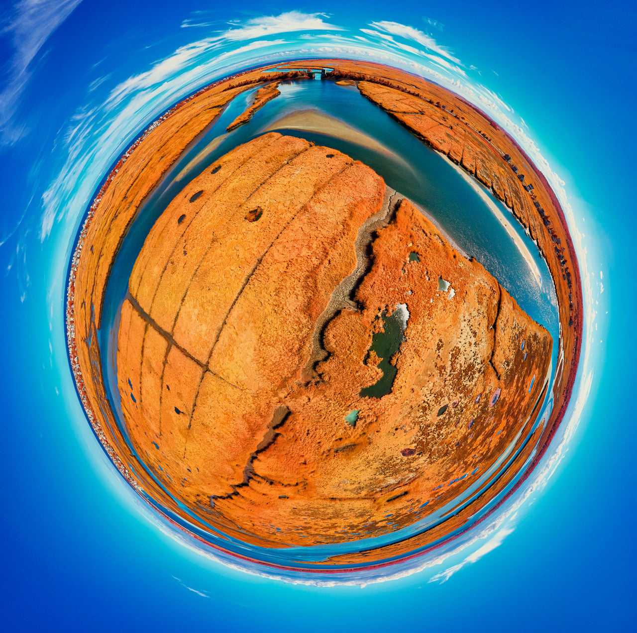 A 360-degree color infrared panoramic photograph of a salt marsh from the Merrimack River in Massachusetts, showcasing vivid orange vegetation and bright blue waters, all encased within a sphere against a clear sky.