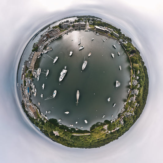 Alt text:
360-degree “tiny planet” image of Woods Hole, Massachusetts, showing a circular harbor filled with moored boats, surrounded by docks, research buildings, houses, and trees under a pale gray sky.
